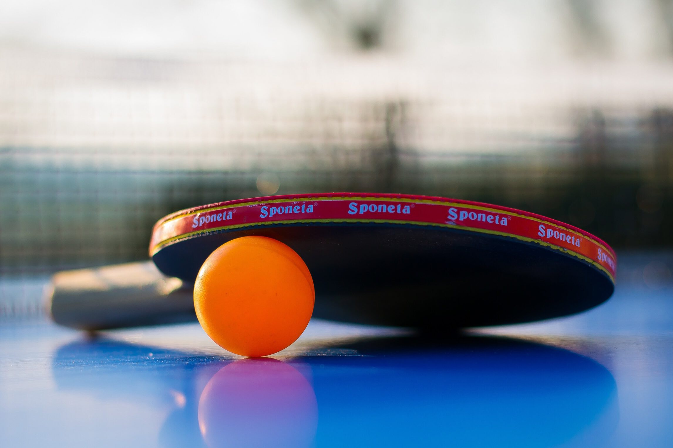Tischtennisschläger mit orangefarbenem Ball auf einer blauen Tischtennisplatte