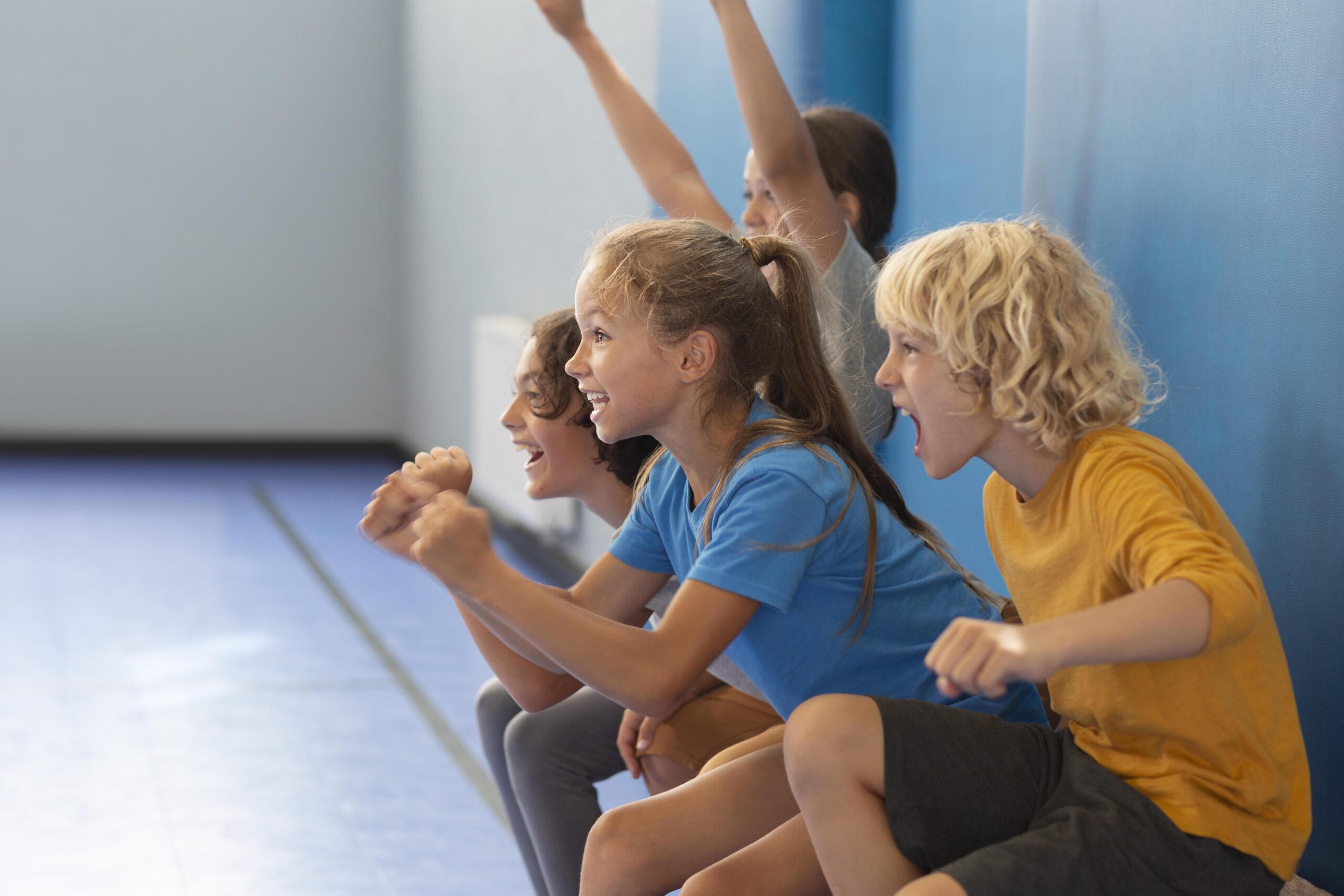 Lachende Kinder in Sportkleidung sitzen auf einer Bank in der Turnhalle